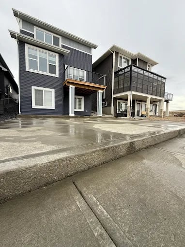 Modern two-story home with dark blue siding, concrete patio, and large windows